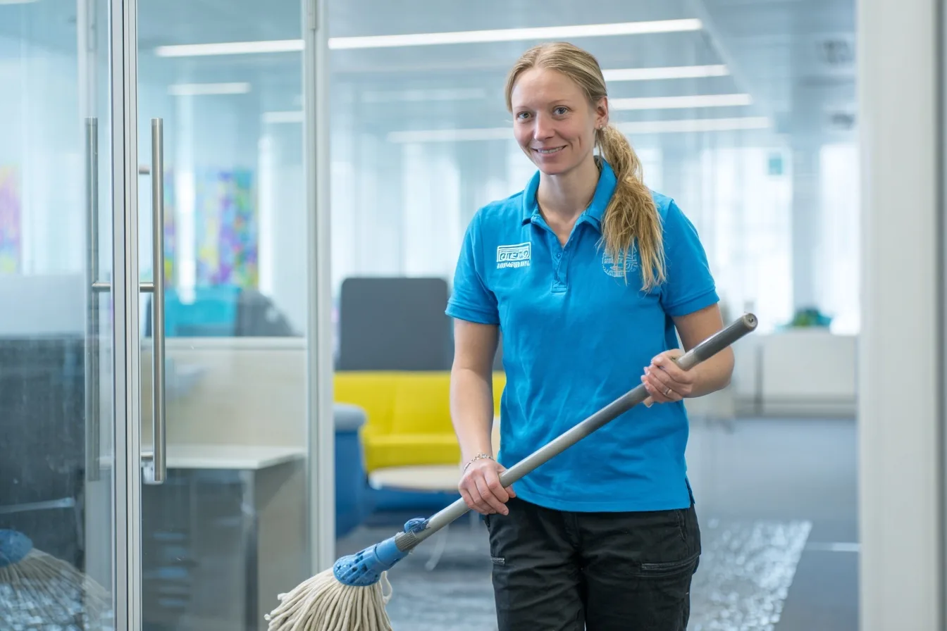 Professionell städare gör rent modernt svenskt kontor med golvmopp